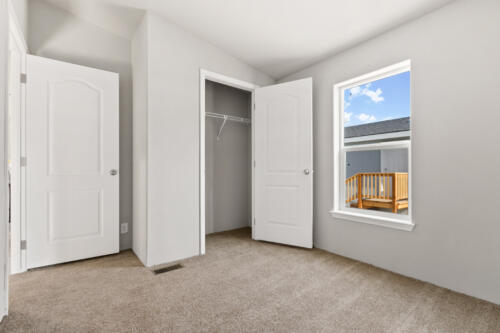 An empty room with white closet doors and tan carpet.