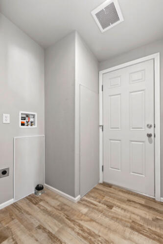 A hallway with a white door and wood floor.