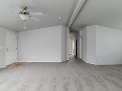 Empty living room with gray carpet and ceiling fan.