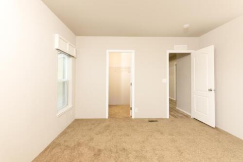 An empty room with tan carpet and white doors.